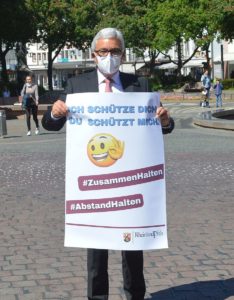 Innenminister Roger Lewentz mit Mundschutz und Plakat zu Abstand und Zusammenhalt. - Foto: gik