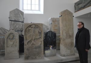 Der ehemalige Chef der GDKE, Thomas Metz, mit einigen antiken römischen Grabsteinen, die in der Lobby des Interim-Landtags präsentiert werden. - Foto: gik
