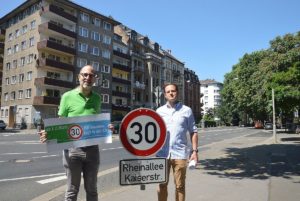 Die Ortsvorsteher Brian Huck und Christopher Hand (beide Grüne) mit Tempo 30-Schild an der Mainzer Rheinallee. - Foto: gik