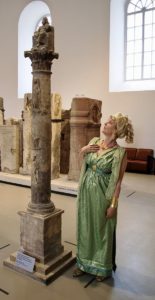 Eine Stadtführerin im römischen Kostüm mit der antiken Jupitersäule. - Foto: GDKE