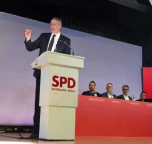 Rede von Alexander Schweitzer (SPD) am Samstag auf dem Parteitag der SPD Rheinland-Pfalz in Nieder-Olm. Im Hintergrund rechts (von links): Staatssekretär Daniel Stich, Innenminister Michael Ebling und Landtagspräsident Hendrik Hering. - Foto: SPD RLP